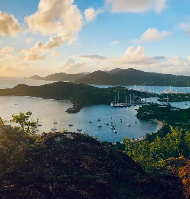 Sailboats anchored in a sheltered harbour surrounded by green hills at golden hour, Antigua