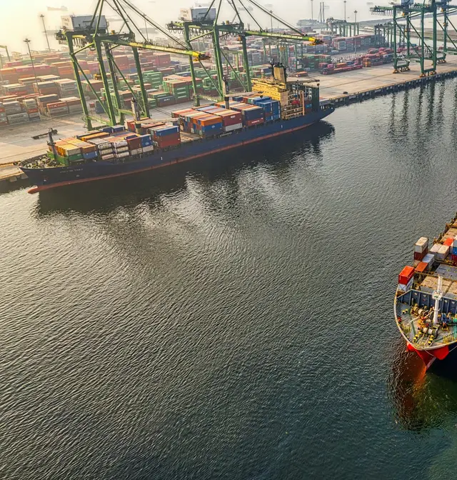 Aerial view of a loaded container ship guided out of port by two tugboats