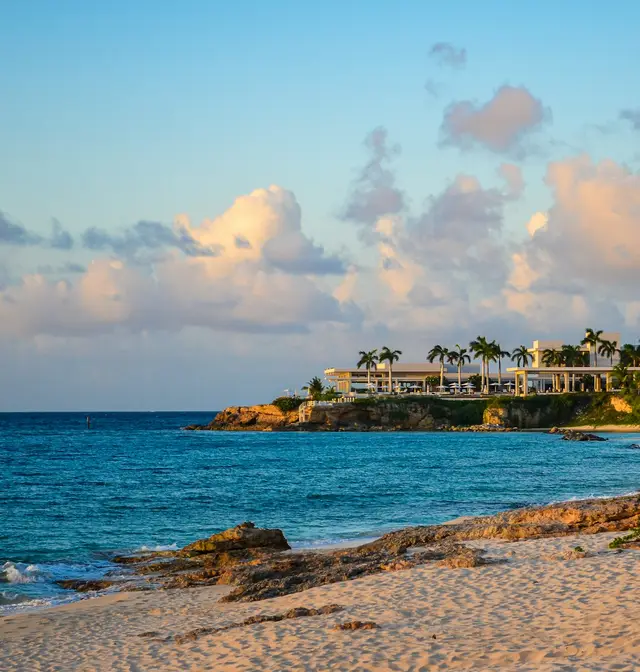 Golden evening light over the sandy beach and rocky point at Barnes Bay, Anguilla, with palm trees and coastal villas