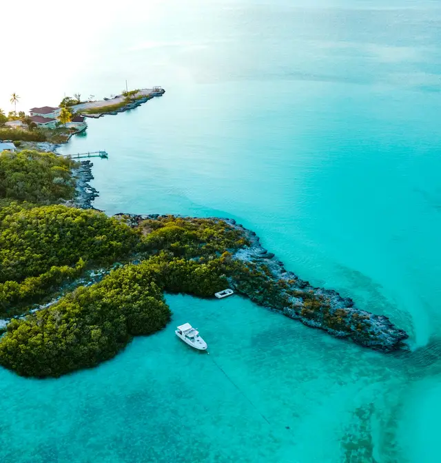 Aerial view of a small wooded island with a villa and bright turquoise shallows in the Exumas, The Bahamas