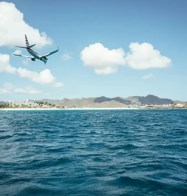 A passenger jet descending over deep blue sea toward the coast of Saint-Martin