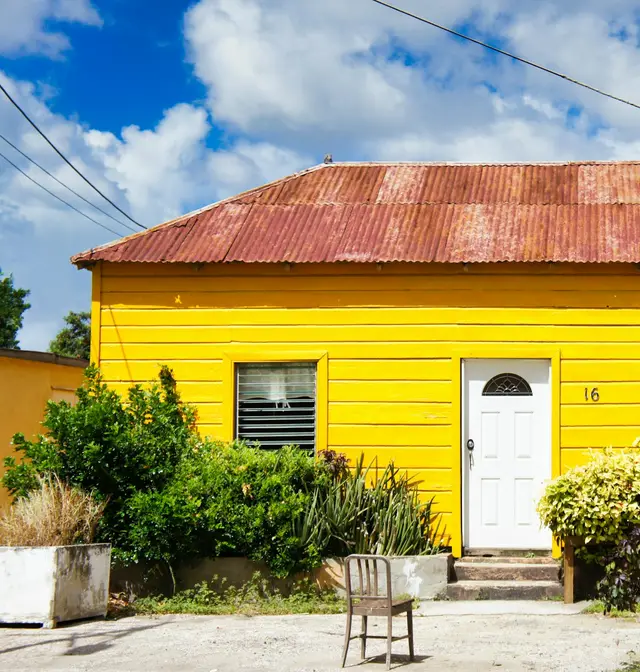A bright yellow wooden house with a red roof and tropical shrubs in Aruba